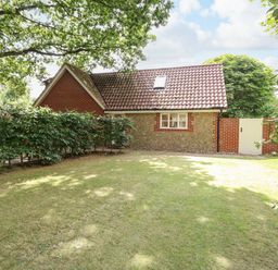 A garden with a lawn and a small house with a tiled roof and brick and stone walls at Oak Tree Lodge in Crostwick near Norwich