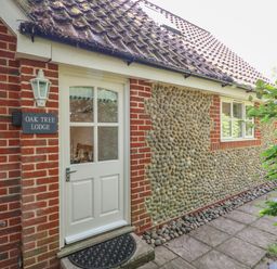An exterior view of a brick and stone cottage with a white door and window at Oak Tree Lodge in Crostwick near Norwich