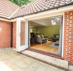 An open door leading from a brick patio to a living room with sofas and wooden floor at Oak Tree Lodge in Crostwick near Norwich