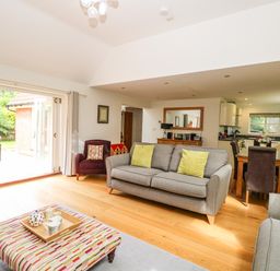 A living room with a grey sofa and green cushions a dining table with chairs and an open doorway to a garden at Oak Tree Lodge Crostwick near Norwich