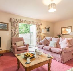 A living room with pink armchairs a wooden coffee table with tea set and fruit bowl and a television at Dorothy's Cottage in Alnmouth