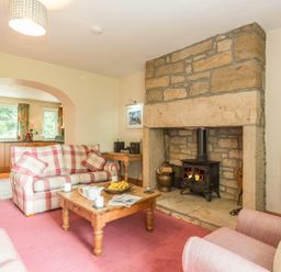 A living room with a stone fireplace wooden coffee table checkered sofa and an open archway to the kitchen at Dorothys Cottage in Alnmouth