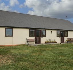 The exterior of a single story building with grass in front and benches near the doors at Brindle Cottage in Royal Wootton Bassett