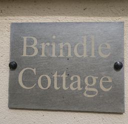 A gray stone plaque with the words Brindle Cottage fixed to a rough beige wall at Brindle Cottage Royal Wootton Bassett