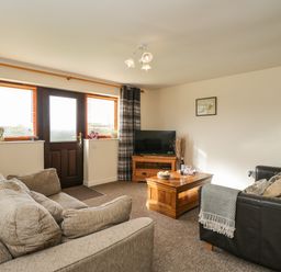 A living room with two sofas a wooden coffee table a television and a door with windows at Brindle Cottage in Royal Wootton Bassett