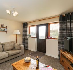 A living room with a sofa coffee table TV and door with windows at Brindle Cottage in Royal Wootton Bassett