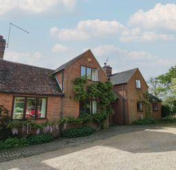 A brick house with a tiled roof and climbing plants by a gravel driveway at Highcroft in Stratford-Upon-Avon
