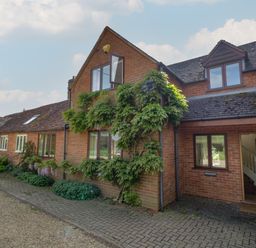 Exterior view of a brick house with plants and a paved pathway at Highcroft in Stratford-Upon-Avon