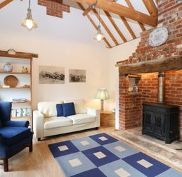 A living room with a blue armchair white sofa rug and brick fireplace at Stable Cottage in Necton near Swaffham
