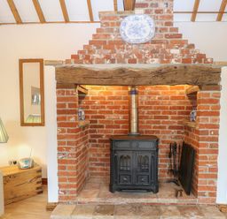 A brick fireplace with a wood stove and a wooden beam mantel with a decorative plate above at Stable Cottage in Necton near Swaffham