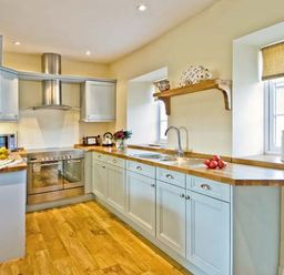A kitchen with wooden countertops, white cabinets, double oven, stainless steel hood, and windows at The Old Farmhouse in Lowick