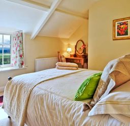 A bedroom with a bed green cushion dressing table and floral curtains at The Old Farmhouse in Lowick