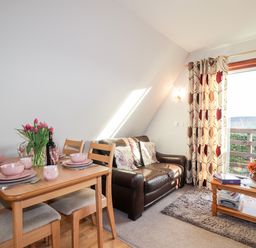 A dining table set with pink dishes and tulips next to a brown leather sofa in a living room with patterned curtains at Larchfield Chalet 2 Heights of Achterneed near Strathpeffer