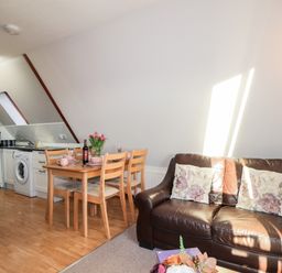 A living area with a brown leather sofa with floral cushions a wooden dining table with four chairs and a kitchen area with appliances at Larchfield Chalet 2 Heights of Achterneed near Strathpeffer