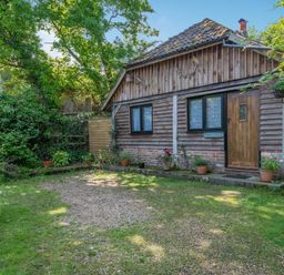 A wooden cabin with a tiled roof and potted plants outside in a garden setting at Endymion Linwood near Ringwood New Forest