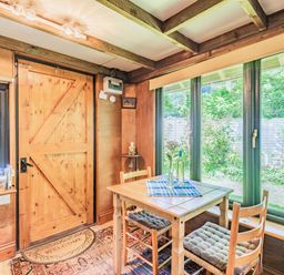 A dining area with a wooden table and two chairs near large windows and a wooden door at Endymion Linwood near Ringwood New Forest