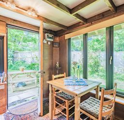A dining area with a wooden table and chairs next to large windows and a door opening to a garden at Endymion Linwood near Ringwood New Forest
