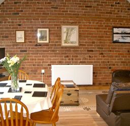 A dining area with a round table and wooden chairs and a living space with leather sofas against a brick wall at Happy Union Stables in Abbeycwmhir near Rhayader
