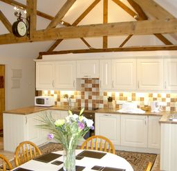 A kitchen with wooden beams white cabinets a dining table with flowers and wooden chairs at Happy Union Stables in Abbeycwmhir near Rhayader