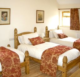 A bedroom with three single beds with red patterned bed runners and cushions at Happy Union Stables in Abbeycwmhir near Rhayader