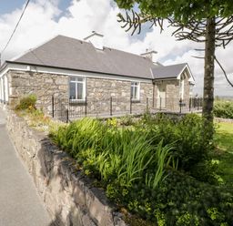 An exterior view of a stone house with a slate roof and a garden with plants and a tree at Prague House in Lettermore County Galway