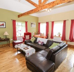 A living room with a leather sofa a red armchair wood beams and a dining table at Prague House in Lettermore County Galway