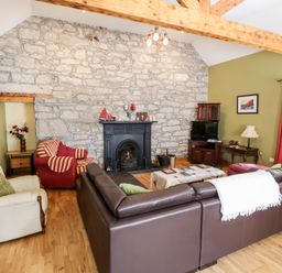A living room with stone wall fireplace brown leather sofa red and cream armchairs wooden furniture and green walls at Prague House in Lettermore County Galway