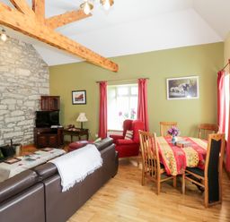 A living room with a stone fireplace wooden beams red curtains and a dining table with chairs at Prague House in Lettermore County Galway