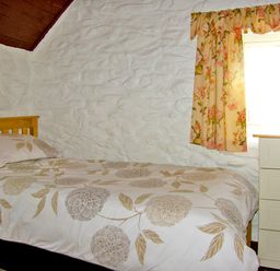 A bedroom with a single bed with floral bedding and a chest of drawers next to a window with floral curtains at Carthy's Cottage Kilbrien near Dungarvan County Waterford