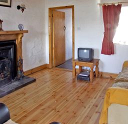 A living room with a fireplace a wooden floor a small table with a TV and a sofa with curtains at Delia's Cottage in Ballinrobe County Mayo