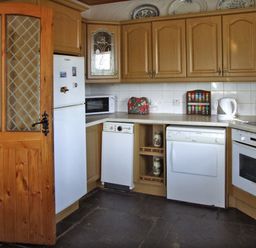 A kitchen with wooden cabinets white appliances a microwave a kettle and spice rack at Delia's Cottage in Ballinrobe County Mayo