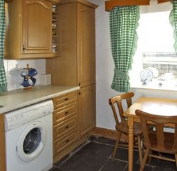 A kitchen with wooden cabinets a washing machine a wooden table and chairs with green check curtains at Delia's Cottage in Ballinrobe County Mayo