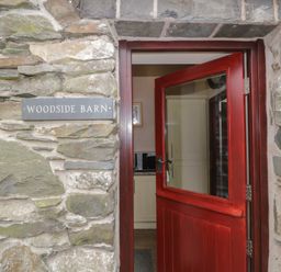 A red half-glass door open on a stone wall with a sign reading Woodside Barn Pennington near Ulverston