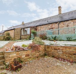 A stone house with a sloped roof and fenced porch with garden beds and gravel pathways at The Stable in Milton near Brampton