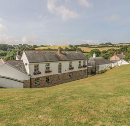 A stone and white house with flower boxes on windows surrounded by a grassy hill and countryside at Chapel Green in Polgooth