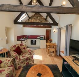 A living area with floral upholstered chairs and a wooden coffee table next to a small kitchen with a dining table and chairs at Barn Cottage High Normanby near Robin Hood's Bay