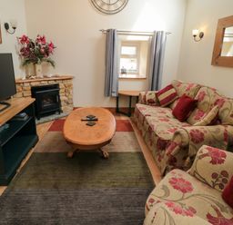 A living room with floral sofas a wooden coffee table a television and a stone fireplace at Barn Cottage in High Normanby near Robin Hood's Bay