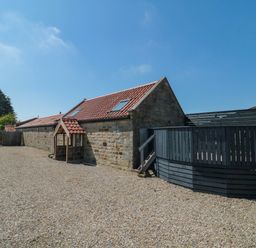 Stone building with tiled roof skylights and black wooden fence on gravel ground at Barn Cottage High Normanby near Robin Hoods Bay