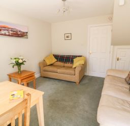 A living room with sofas a wooden table with a book and flowers on a side table at Bramble Cottage in Sedbergh