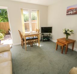 A living room with a dining table and chairs a television and side tables with flowers at Bramble Cottage in Sedbergh