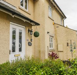 The exterior of a beige house with a white door and windows with plants in front at Bramble Cottage Sedbergh