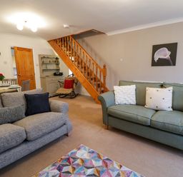 A living room with two sofas pillows a colorful rug wooden staircase and a rocking chair at No 1 Railway Cottages in Betws-y-Coed