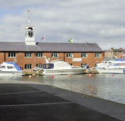 Boats docked in front of a brick building with a clock tower near a waterfront