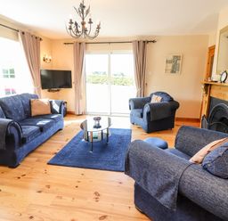 A living room with blue sofas a glass coffee table a fireplace and a wall-mounted television at Fern View House Beaufort near Killorglin County Kerry