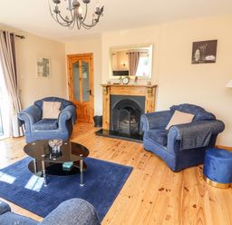 A living room with blue armchairs a glass coffee table a fireplace and wooden floor at Fern View House in Beaufort near Killorglin County Kerry