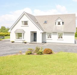 A white house with multiple windows and a grey roof surrounded by grass and a gravel driveway at Fern View House in Beaufort near Killorglin County Kerry