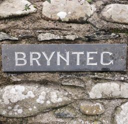 A stone wall with a metal sign reading BRYNTEC at Brynteg Llwyngwril