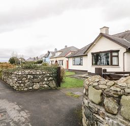 A row of houses with stone walls and a sidewalk along a curved road at Brynteg in Llwyngwril