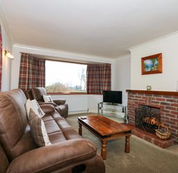 A living room with brown leather sofas a wooden coffee table a brick fireplace and a television at Brynteg in Llwyngwril