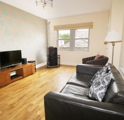A living room with a black leather sofa, striped armchair, television on wooden stand, wood stove, and wooden floor at William Court Cottage Irton Hall near Wastwater